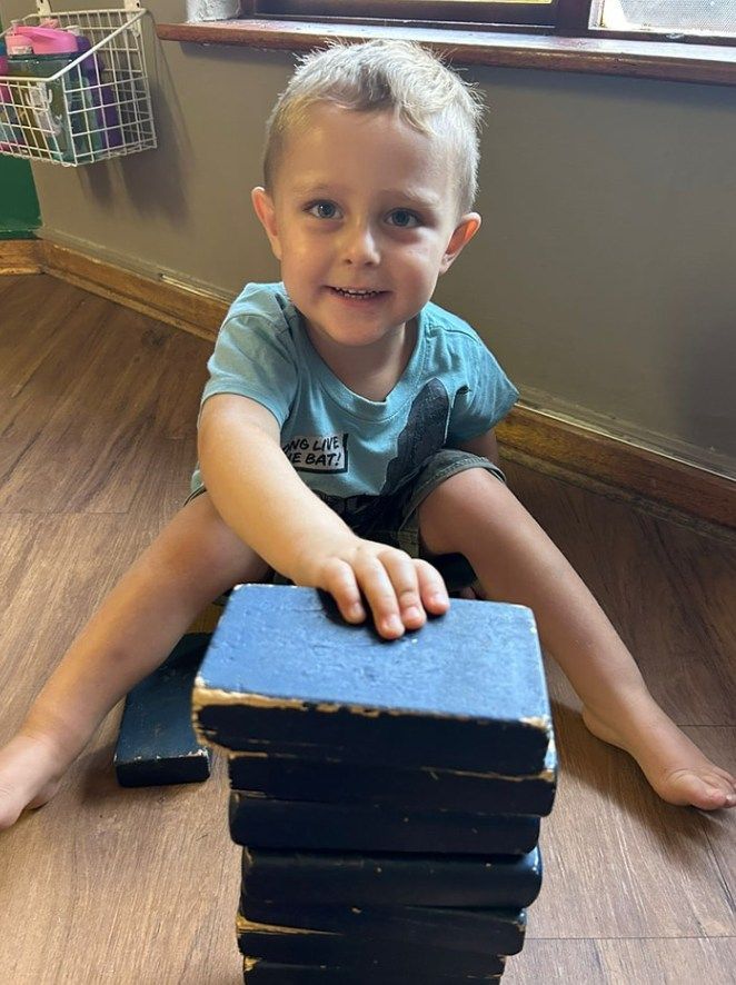 Boy smiling, sitting on floor, stacking books.