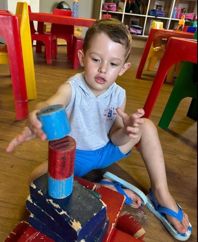 Child building a tower with colorful wooden blocks on a wooden floor in a play area.