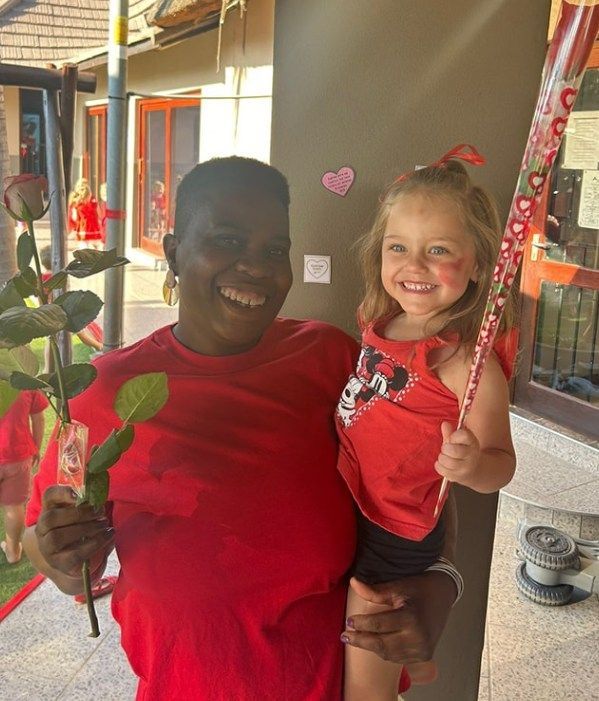 Woman and young girl holding roses, smiling, wearing red, outside.