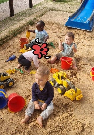 Children playing with sand toys in a sandbox near a blue slide.