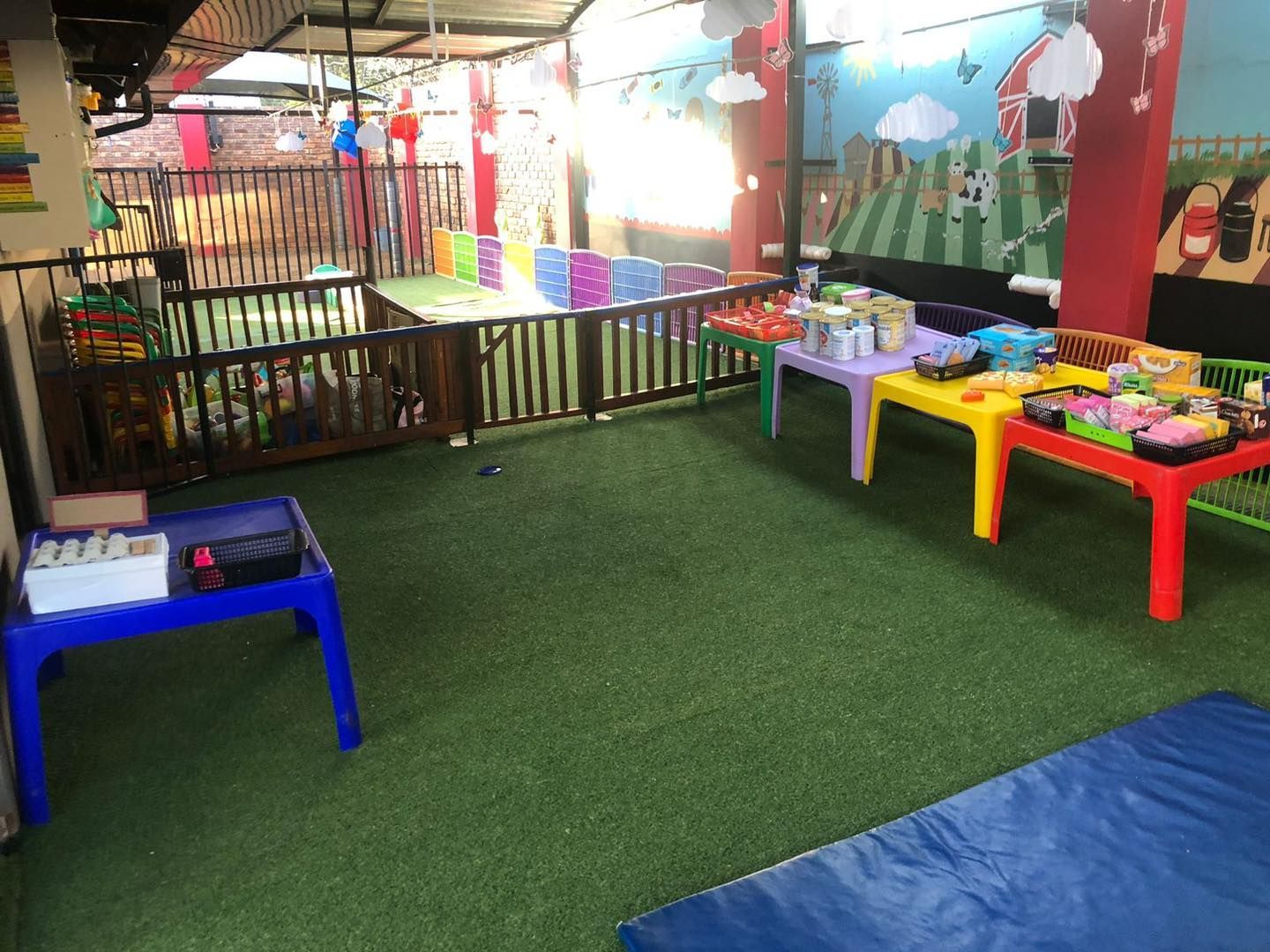 Indoor play area with tables, turf, fence, and painted mural.