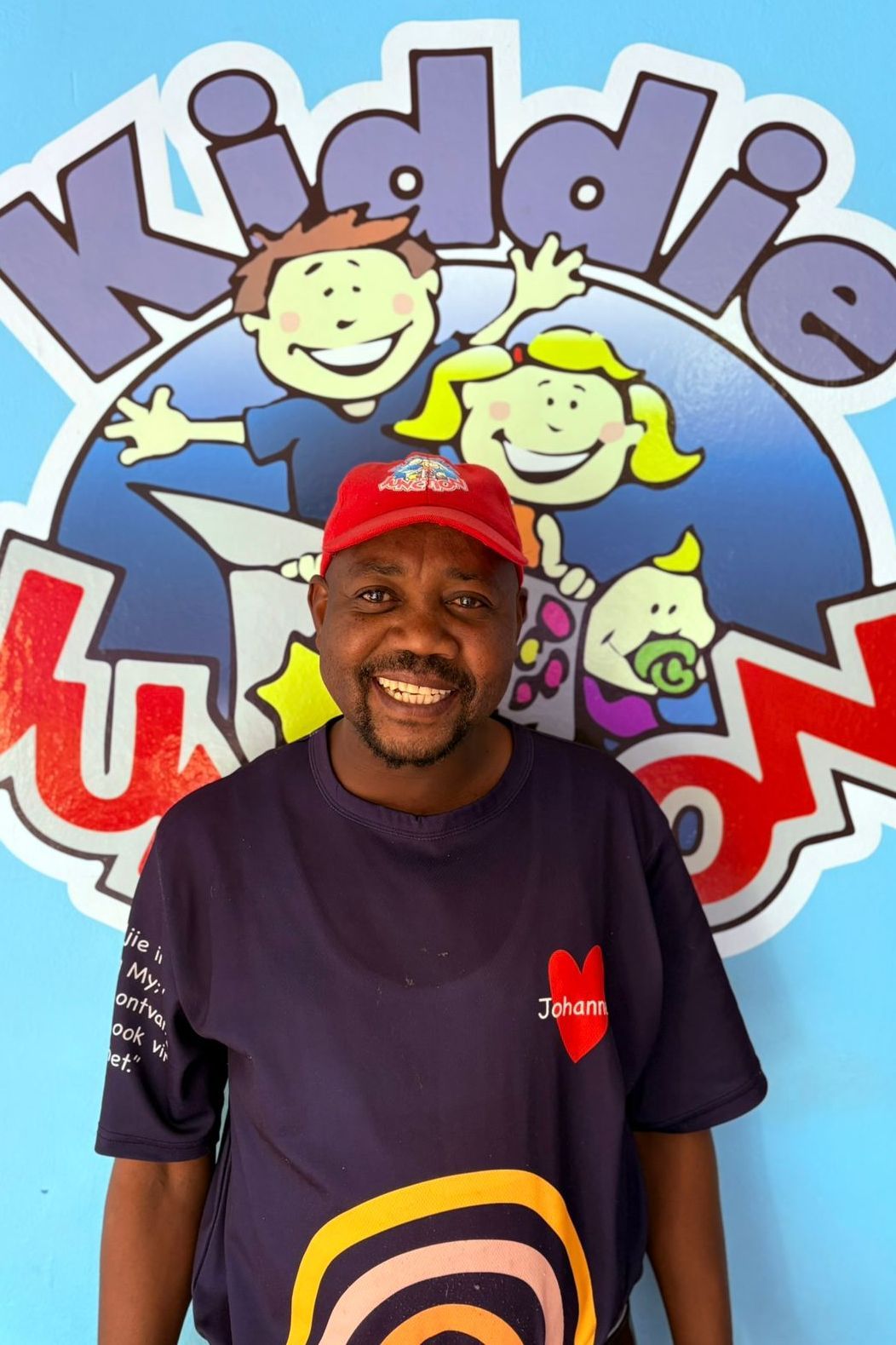Man in red cap and blue shirt smiling in front of a 