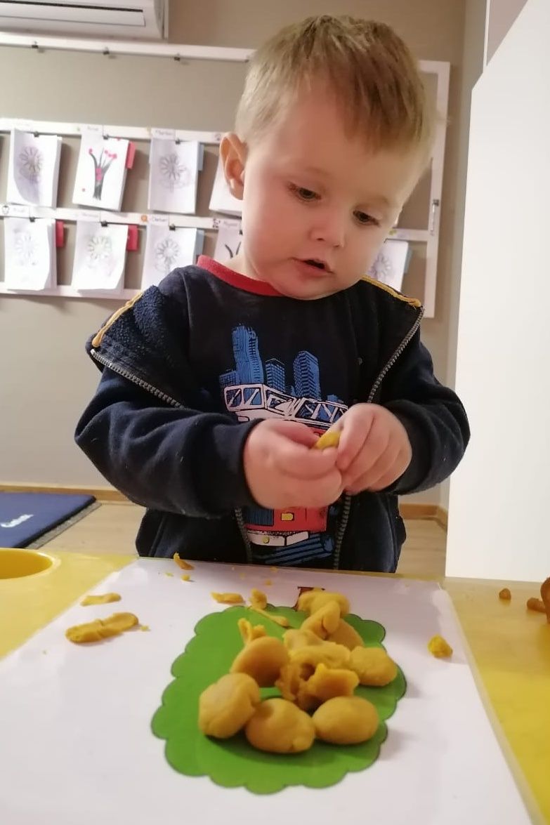 Young child focused on shaping yellow playdough on a green leaf-shaped base.