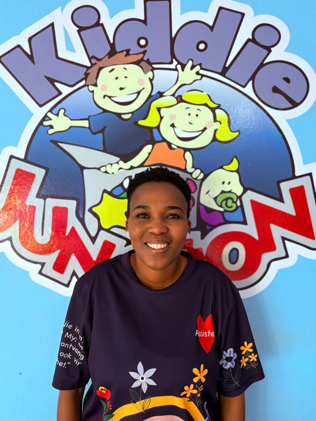 Woman in a navy shirt smiles in front of a blue Kiddie Junction logo on a wall.
