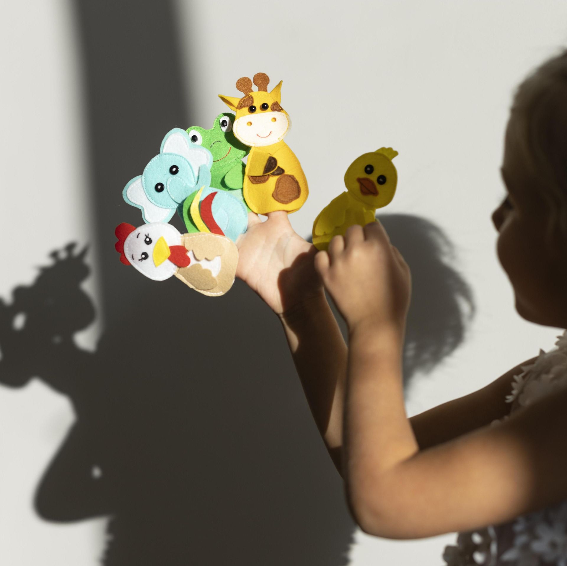 Child playing with animal finger puppets in sunlight.