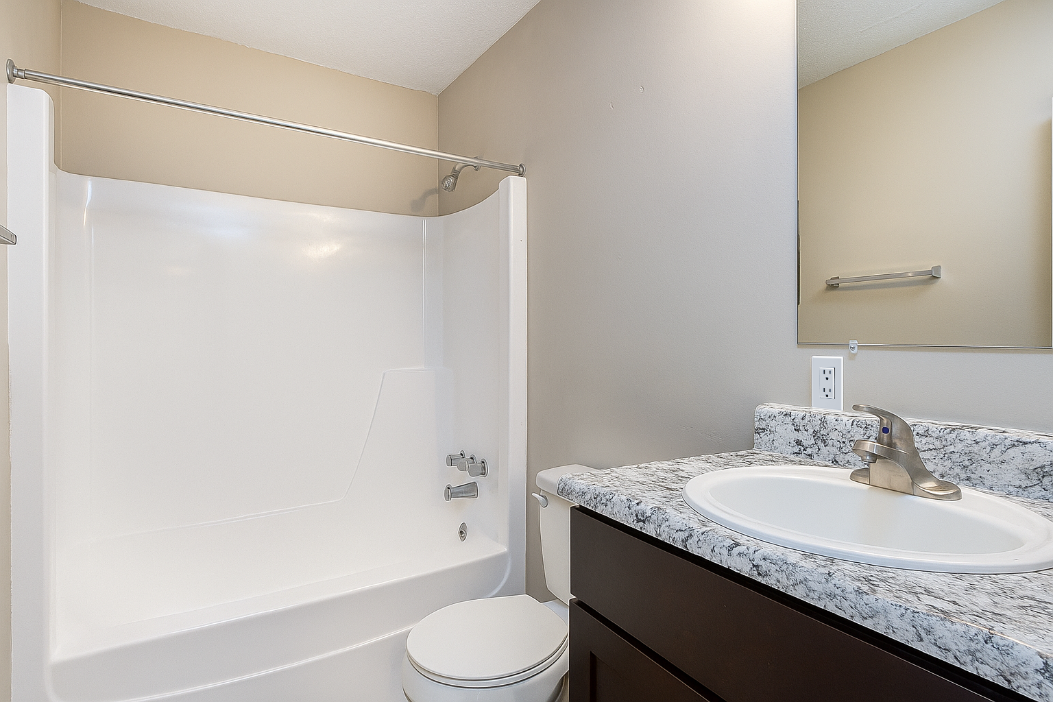 Bathroom with white bathtub, toilet, and sink with speckled countertop, neutral walls.