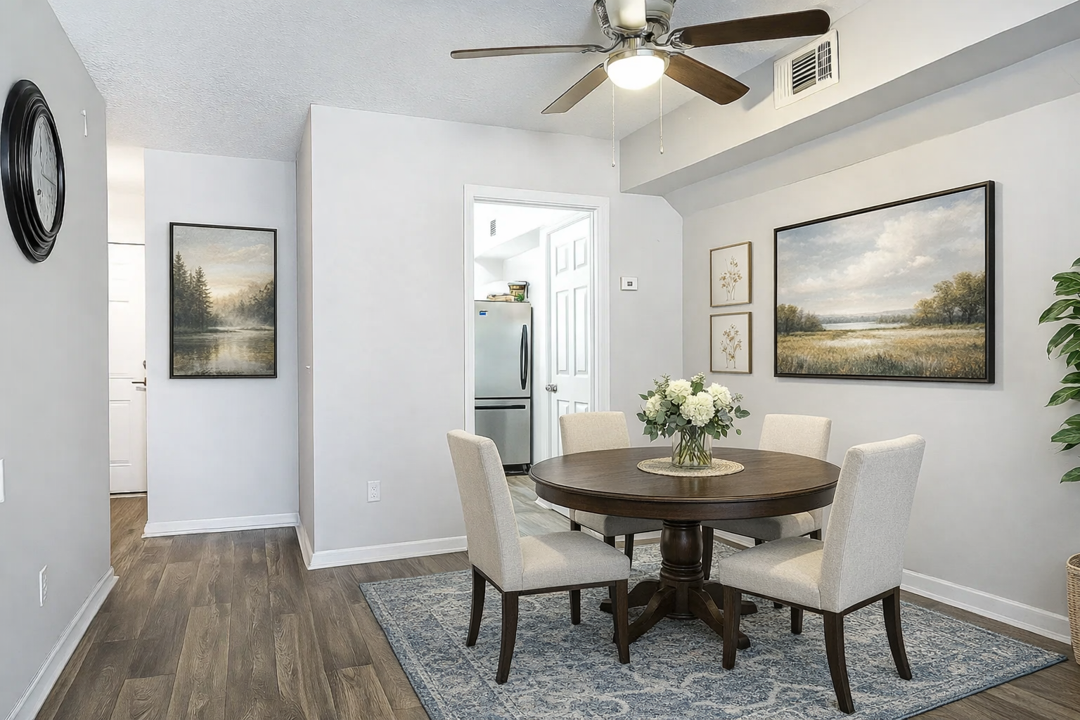 Dining room with round table, chairs, art, rug, and faux plant.