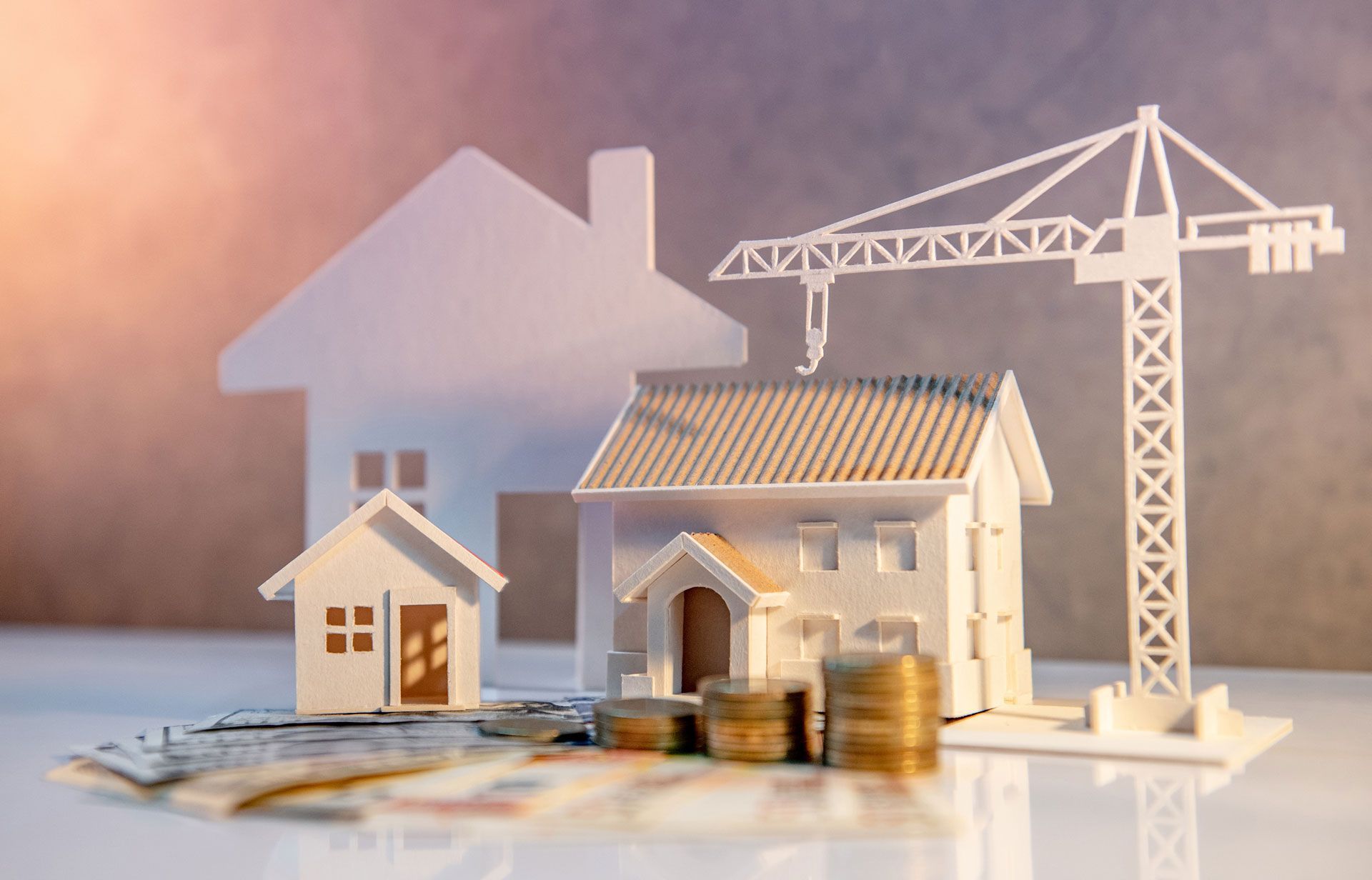 Miniature house, crane, and stacked coins on a table, symbolizing construction and property investment.