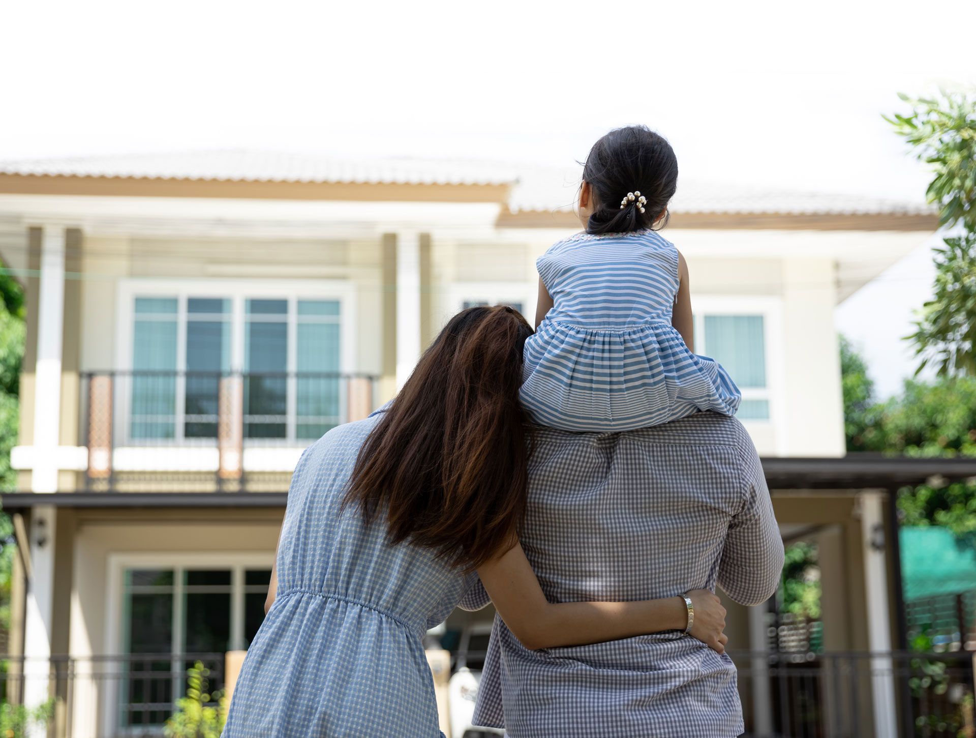 Two people and a child stand outside a modern house, looking toward the home.
