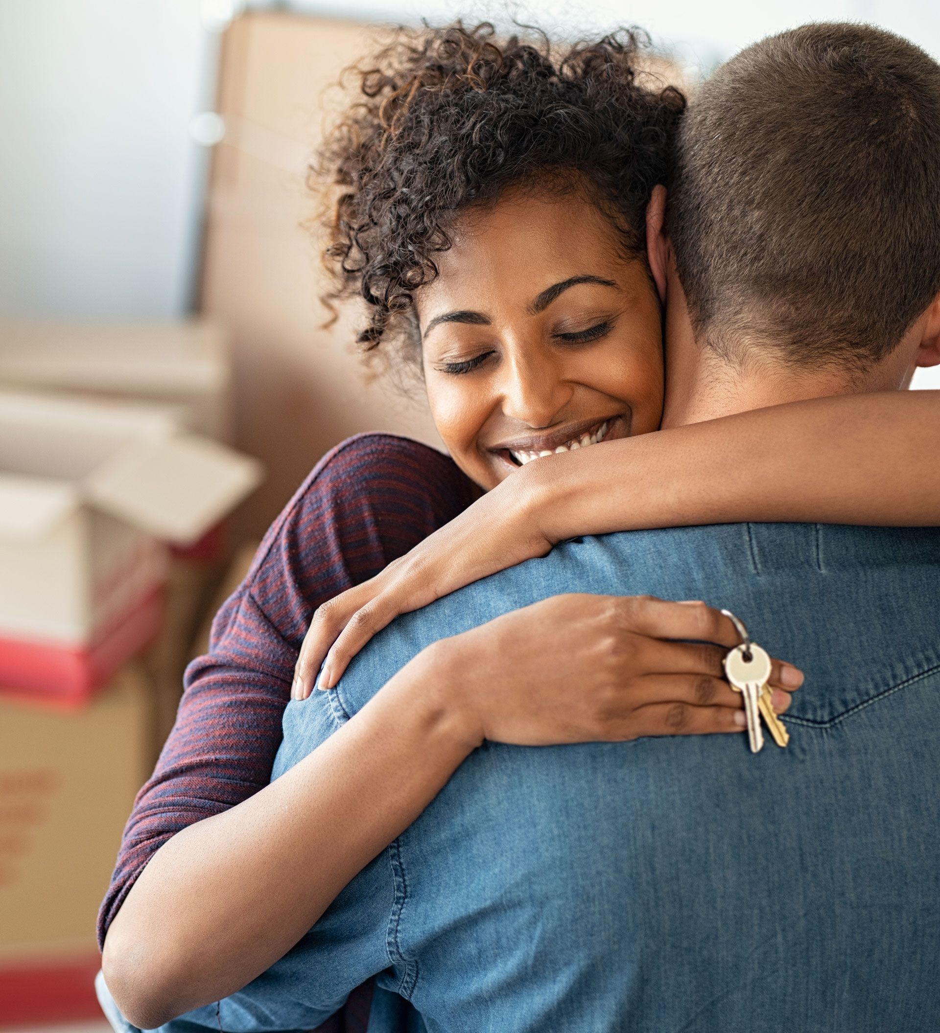 Two people hugging closely indoors, one smiling with keys visible in hand.