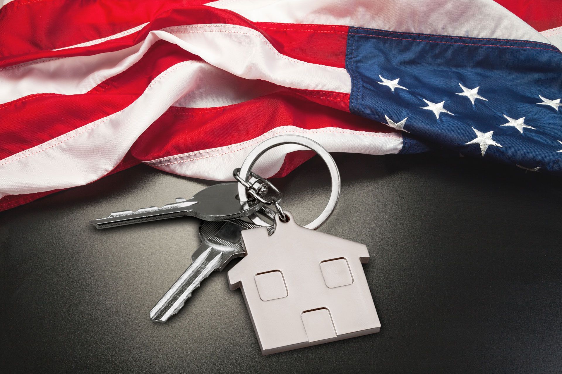 Keys and key fob on a black surface beside a folded American flag.