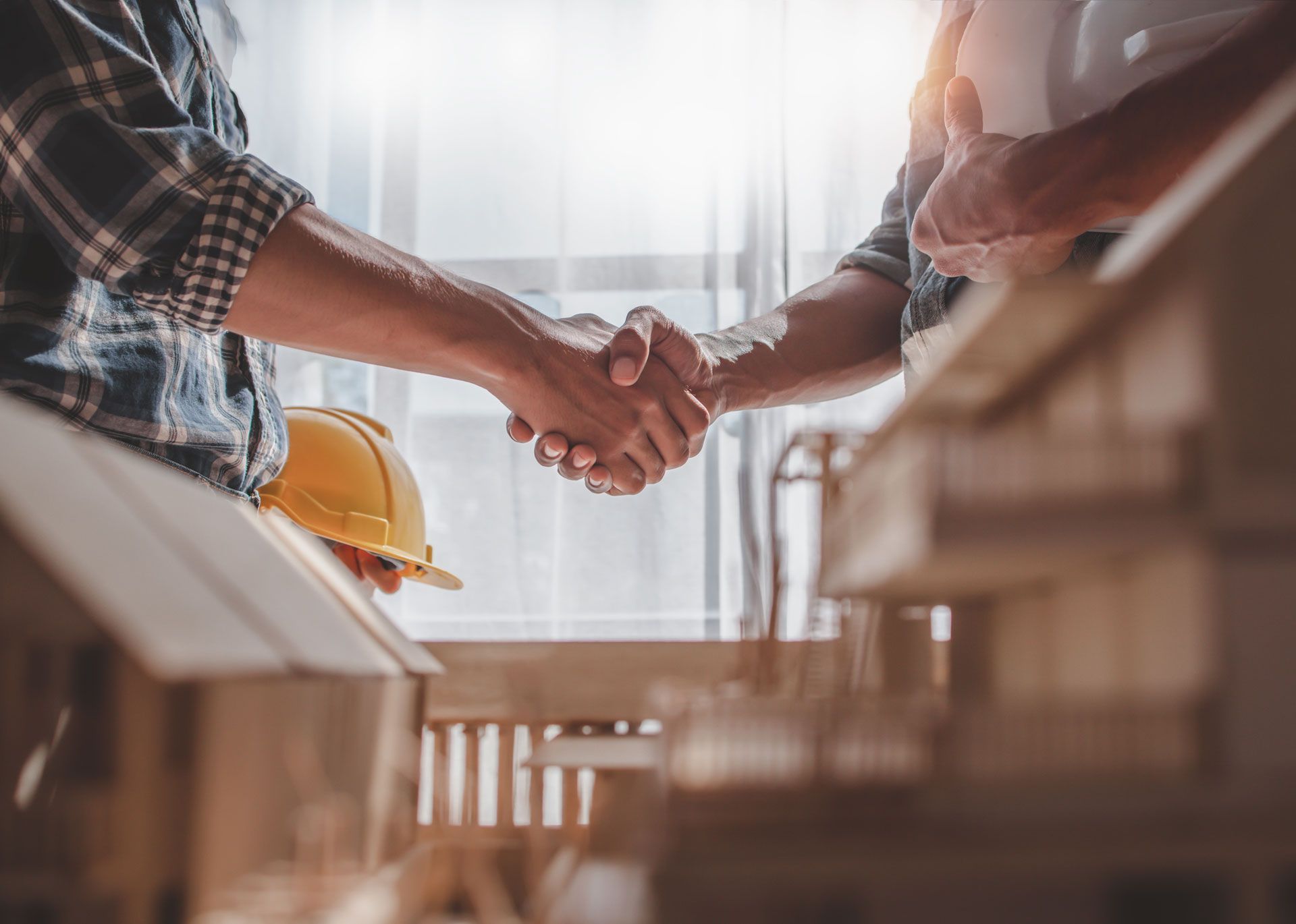 Two workers shaking hands at a construction site, with a hard hat and building materials nearby