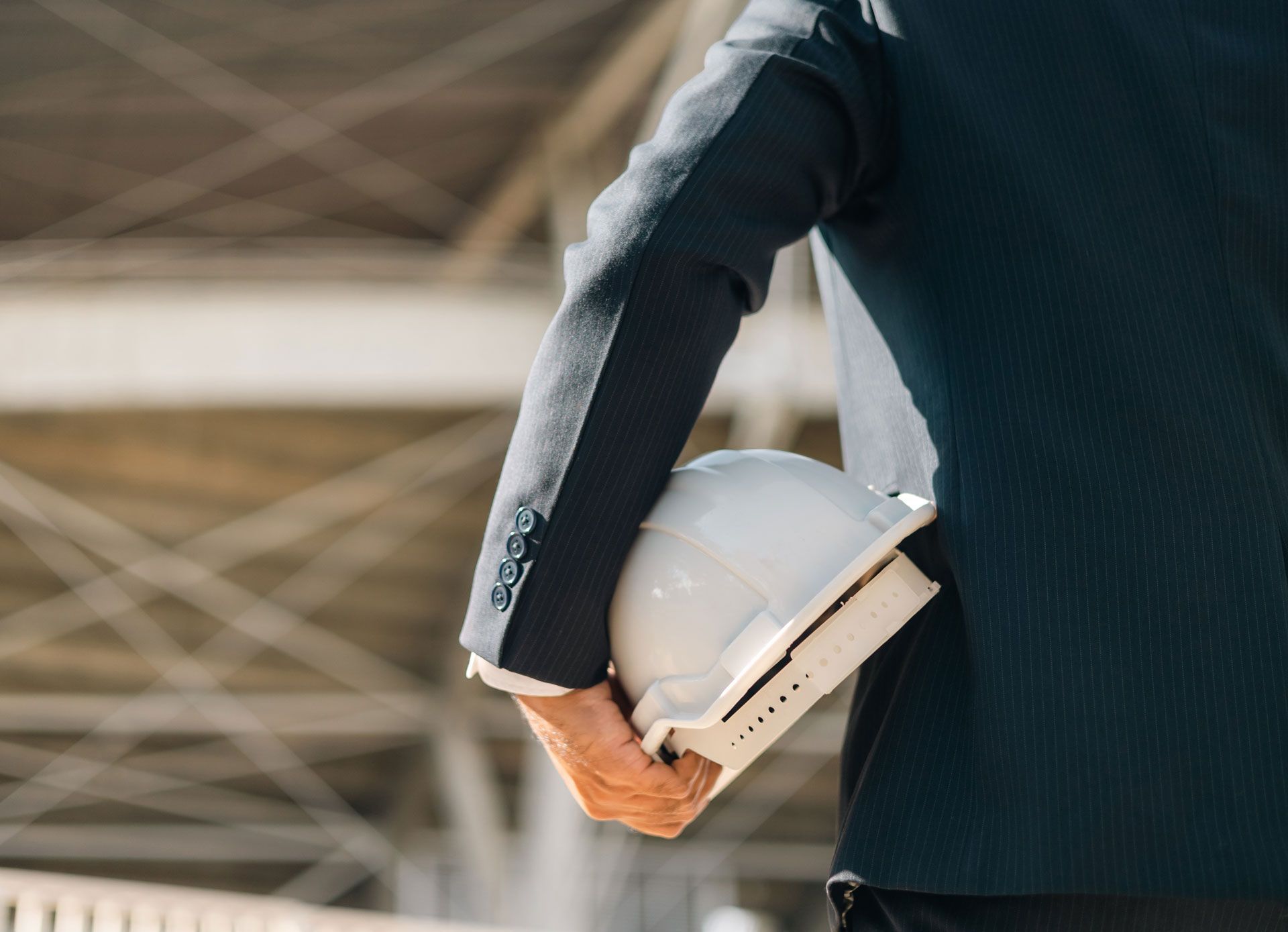 Person in a dark suit carrying a white hard hat at a construction site