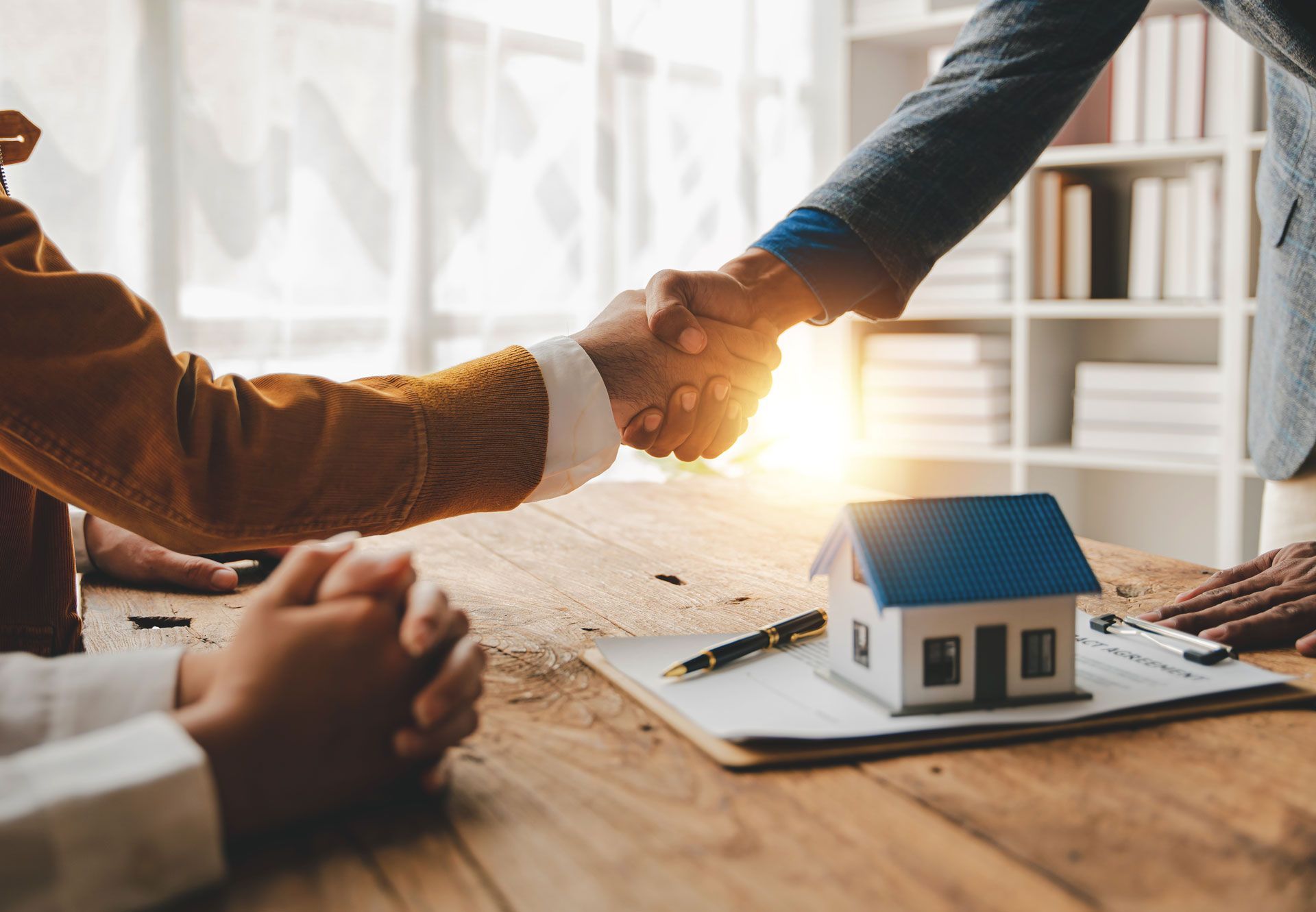 Business handshake over real estate model on a desk in a sunlit office