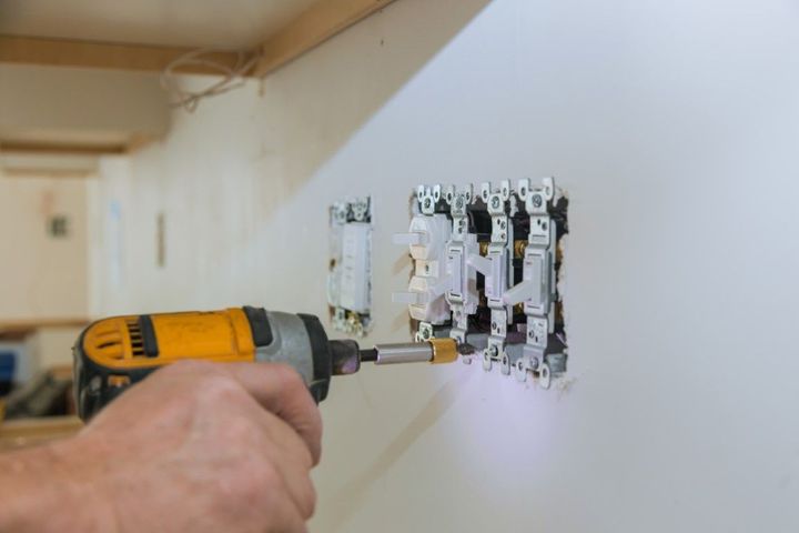 Electrician installing a wall light switch with a cordless drill.