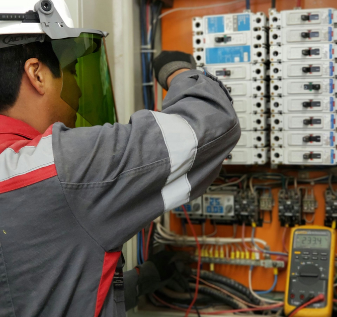 Technician working on a complex electrical panel in hard hat.