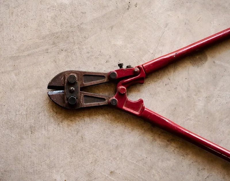 A pair of red bolt cutters laying on a concrete surface.