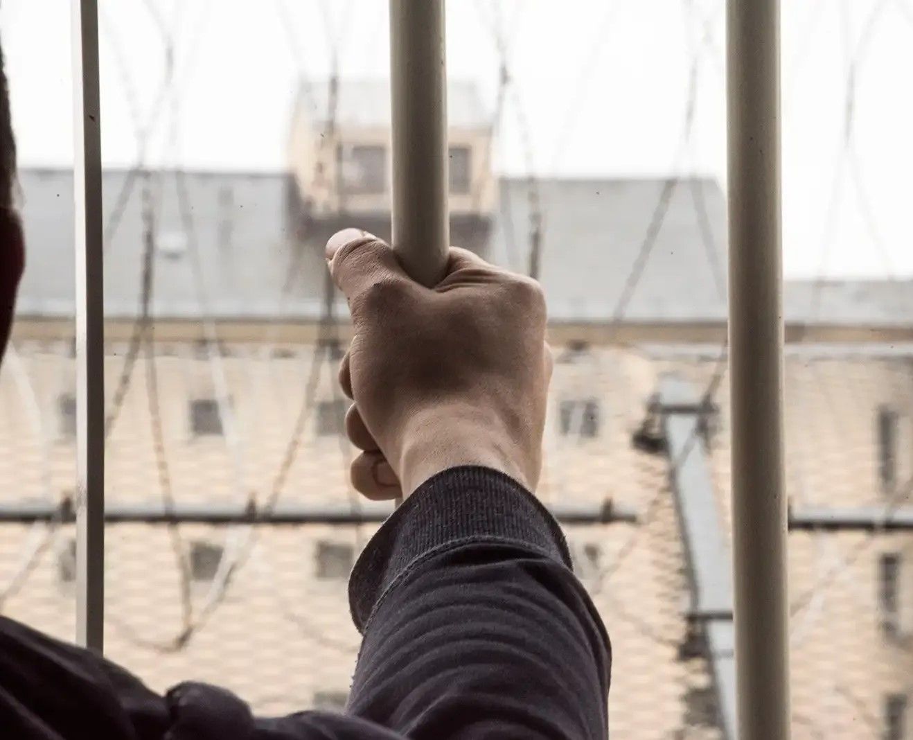 Prisoner's hands gripping the bars of a cell in jail 