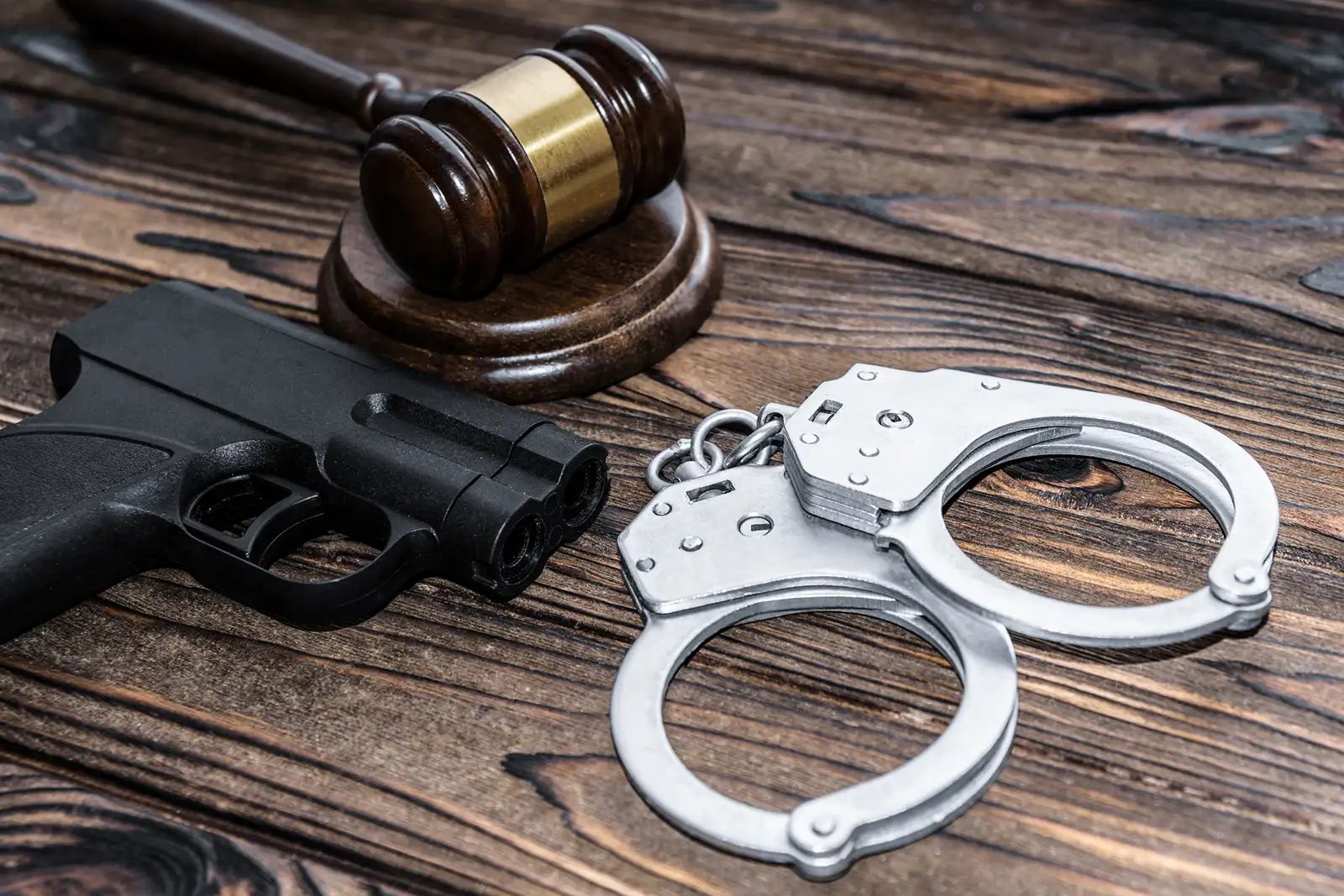 A gun, gavel, and handcuffs in a wood table