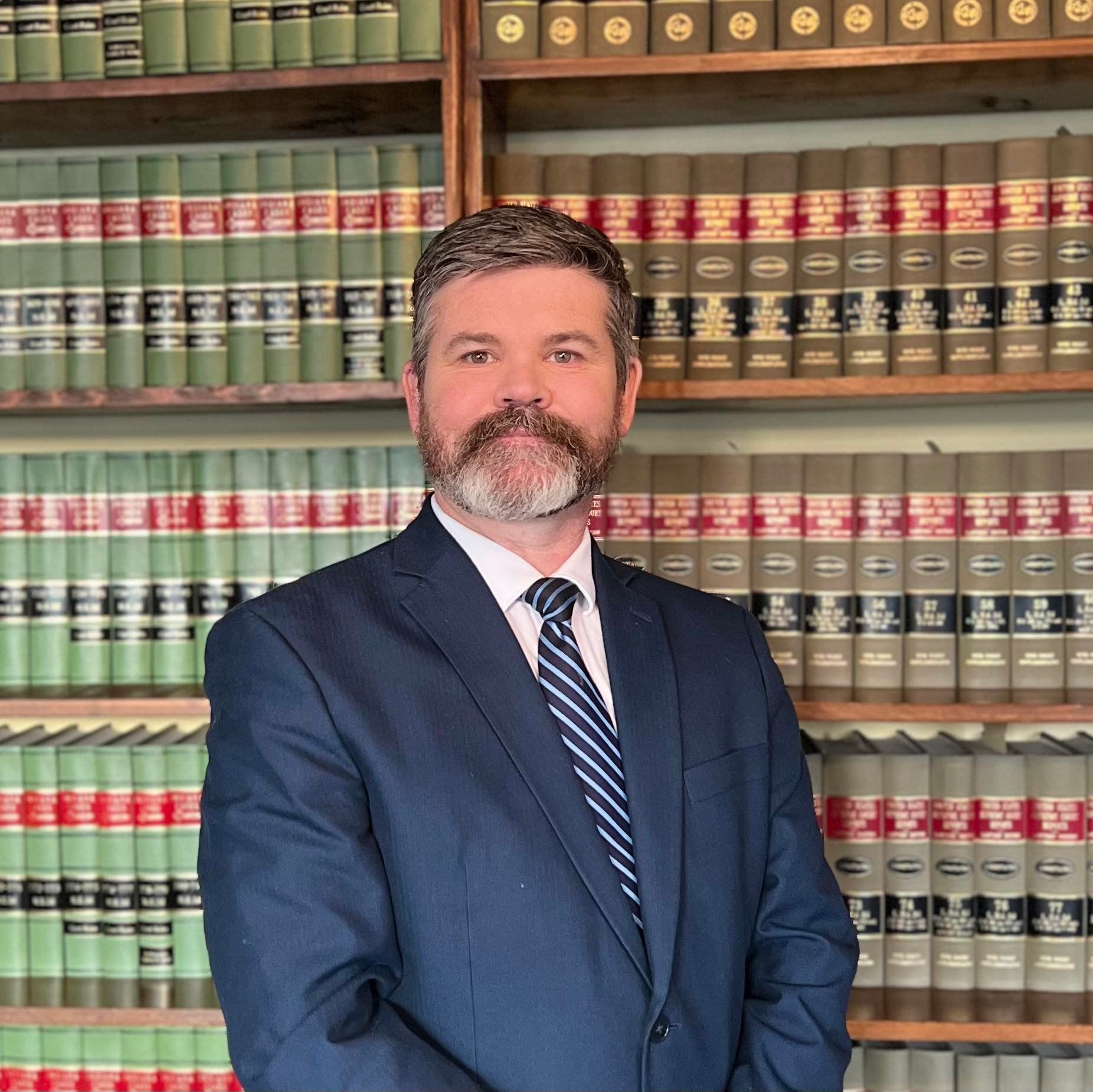 Atty. Ross G. Thomas in a suit and tie is standing in front of a bookshelf filled with books.