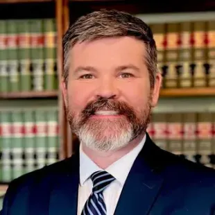 Atty. Ross G. Thomas in a suit and tie is smiling in front of a bookshelf.