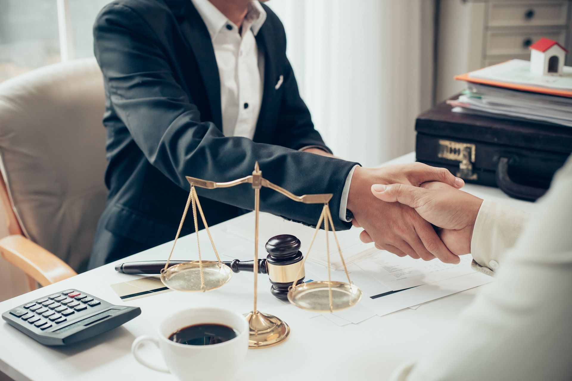 A man and woman are shaking hands over a table with scales of justice.