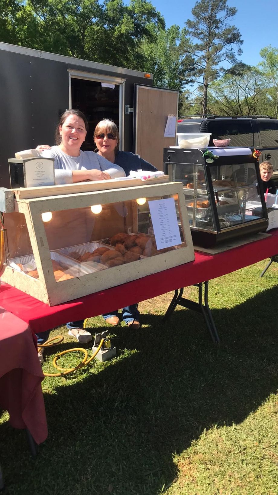 Two people behind a food stall with baked goods, outdoor setting.