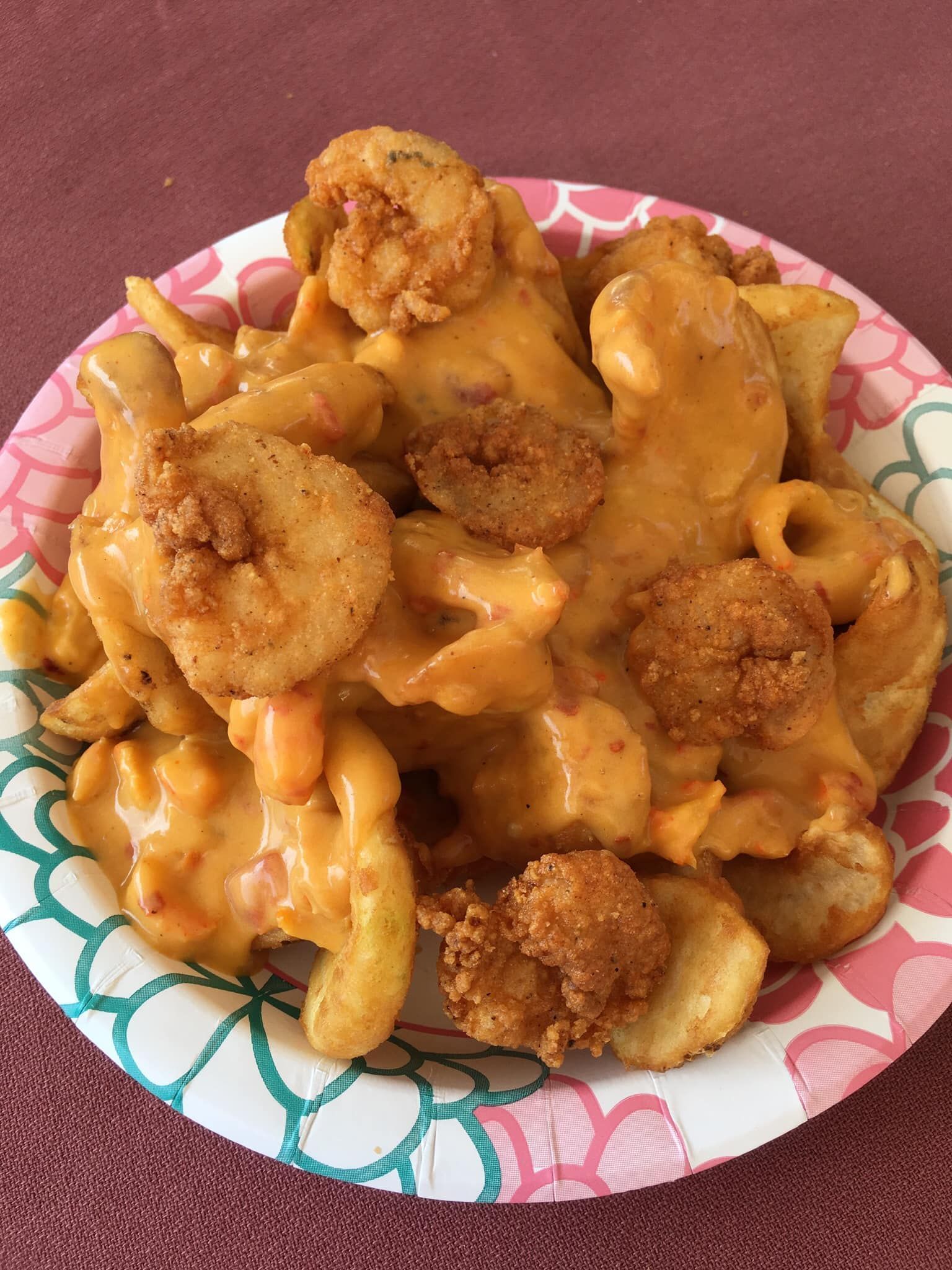 Fried shrimp and potato wedges covered in orange cheese sauce on a paper plate.