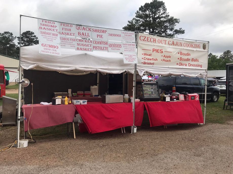 Food vendor stand with red tablecloths and signs, offering items like burgers and sides.