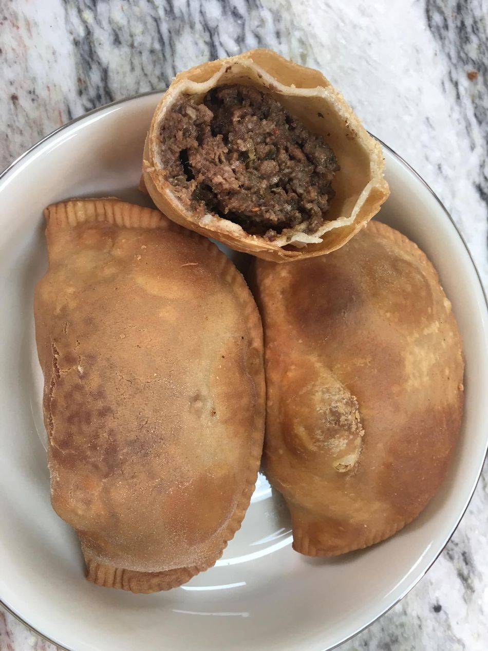 Three golden-brown empanadas in a white bowl, one cut open revealing a savory meat filling.