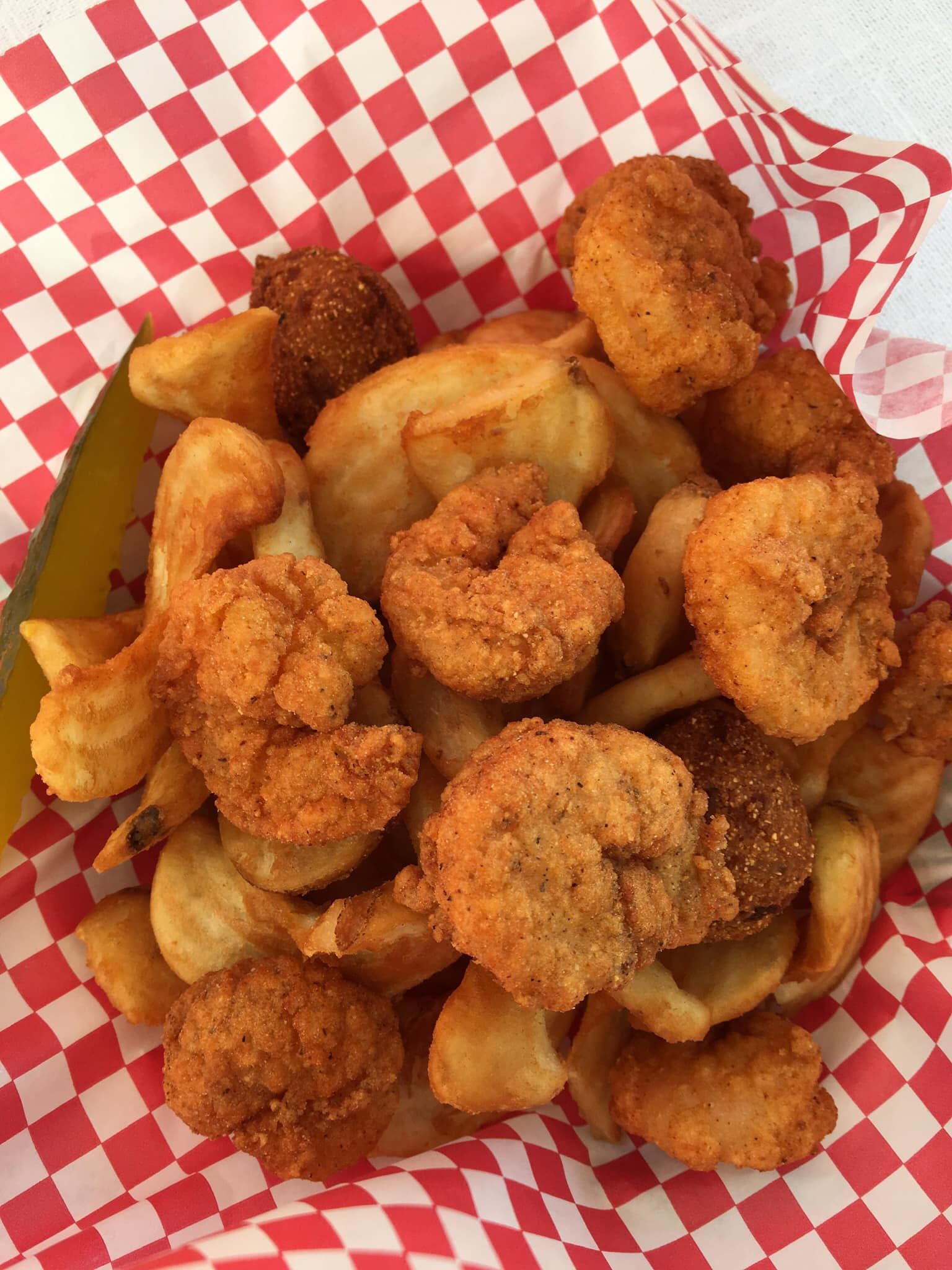 Fried shrimp and potato wedges in a red-checkered basket.