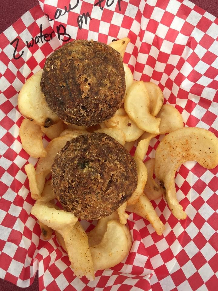 Two brown, fried balls on top of fries, in a red and white checkered basket.