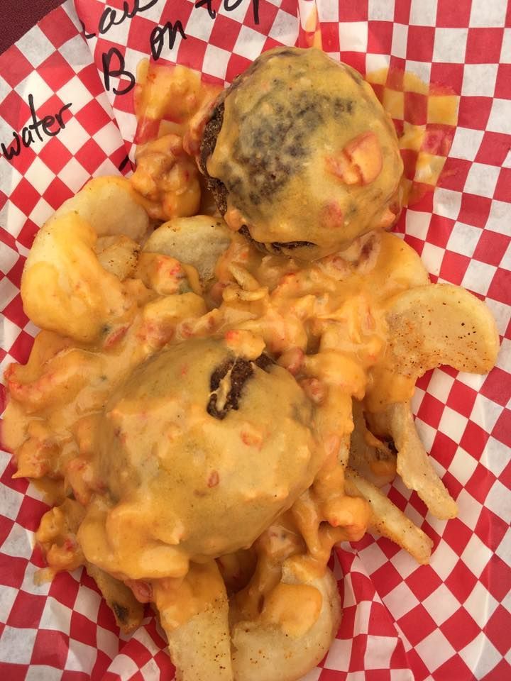Burger and fries covered in orange cheese sauce, on red and white checkered paper.