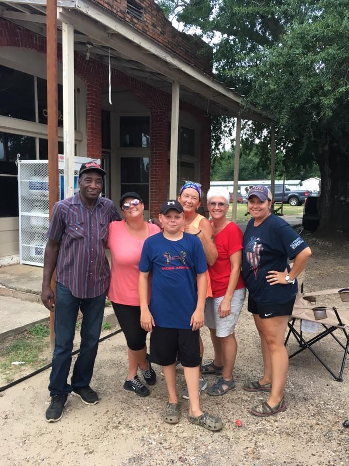 Group of people posing in front of a building; some smiling. Outdoors.
