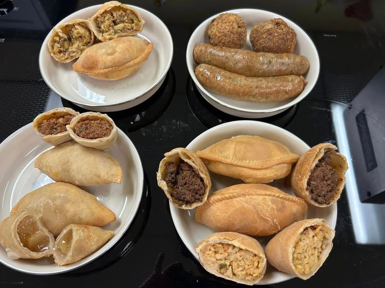 Four plates with assorted savory pastries and sausages on a black surface.