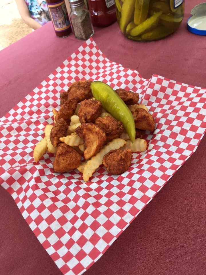 Fried chicken bites and fries on checkered paper with pickle.