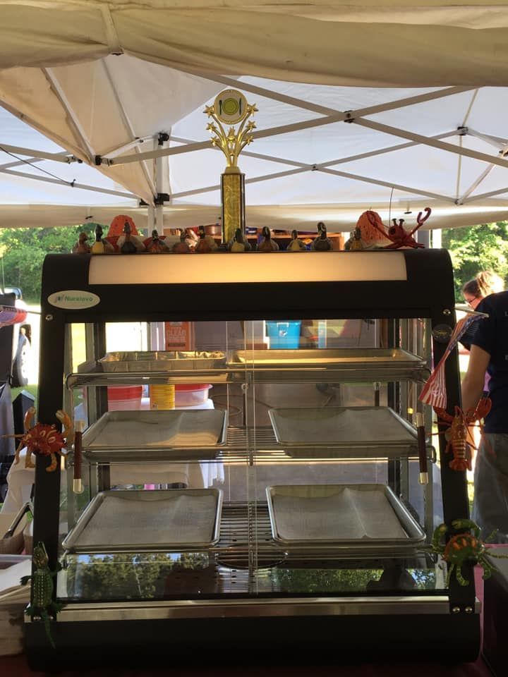 A food display case with empty trays, topped with a trophy and decorations, under a white tent.
