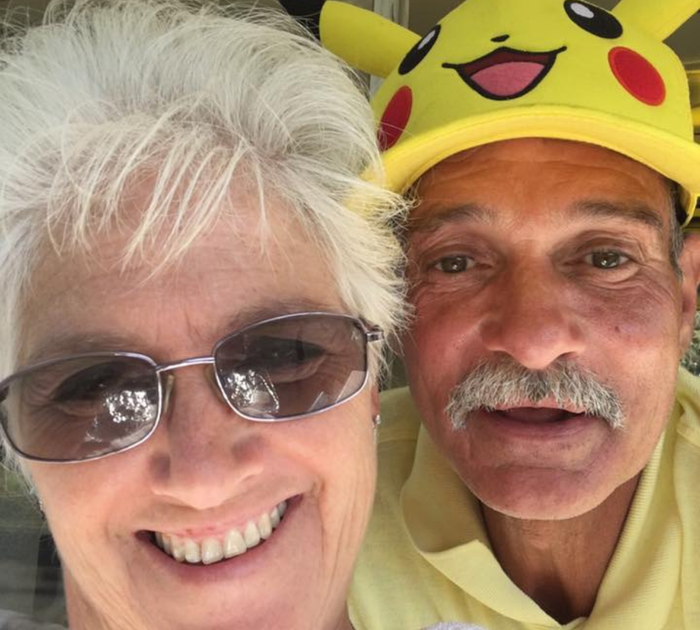 Woman in sunglasses smiles next to a man wearing a Pikachu hat; both are outdoors.