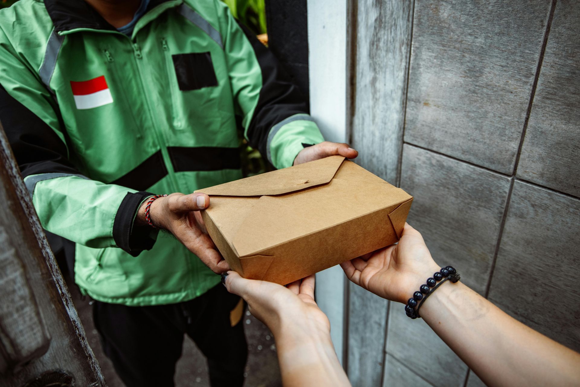 Person in green jacket hands food box to someone at a door.