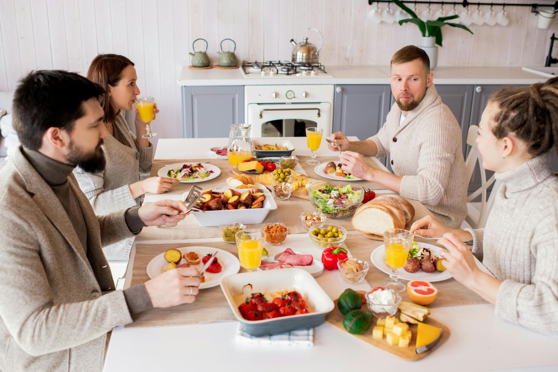 People at a table eating a meal in a kitchen; various dishes and drinks visible.