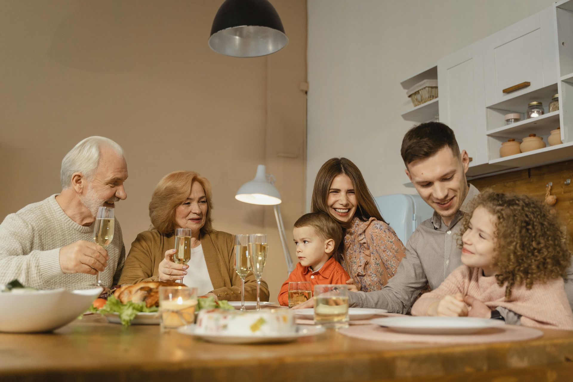 Family celebrating a meal together at a table. People smiling, holding glasses. Indoor setting.