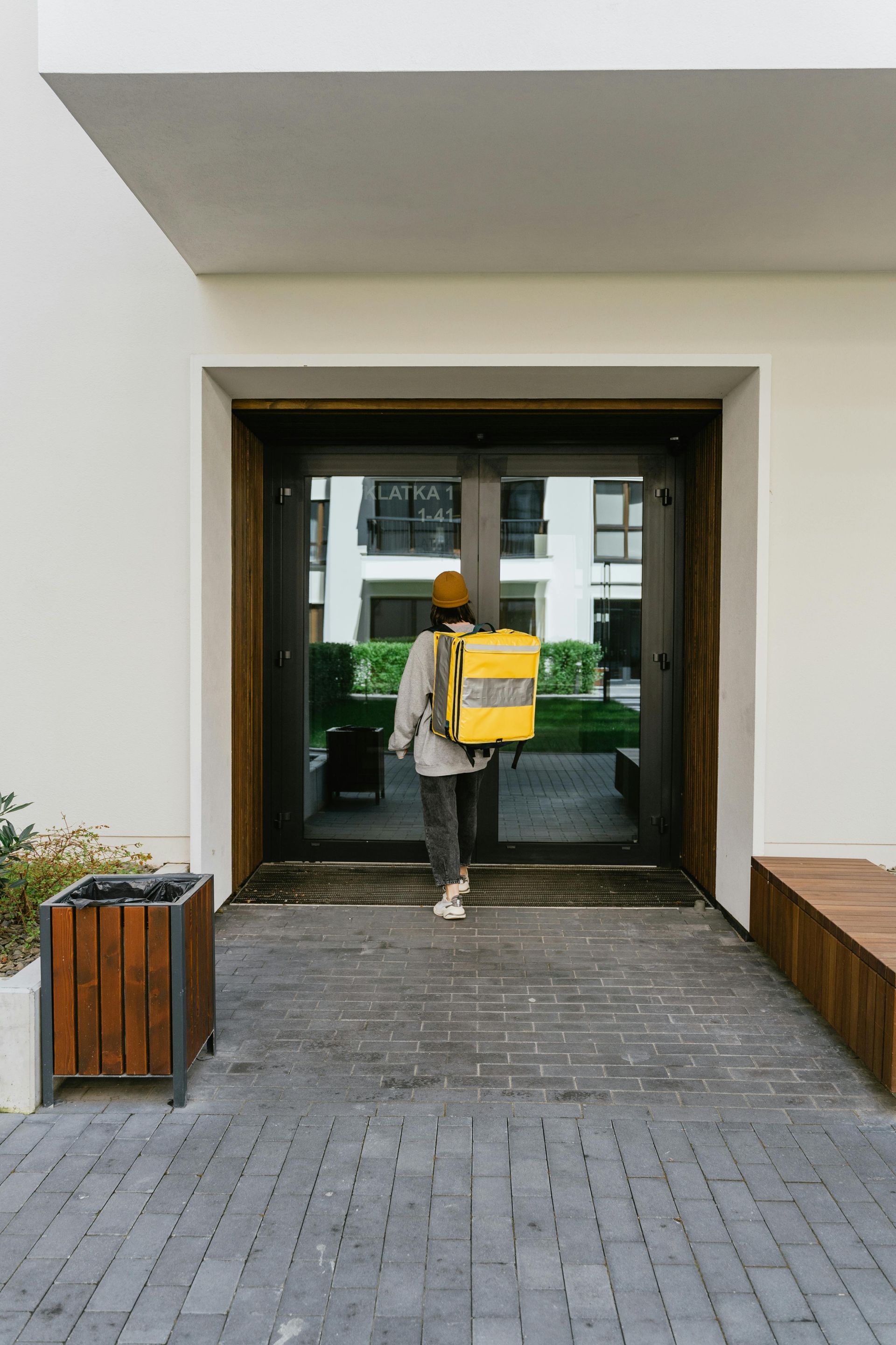 Person with yellow delivery backpack walks through a building entrance.