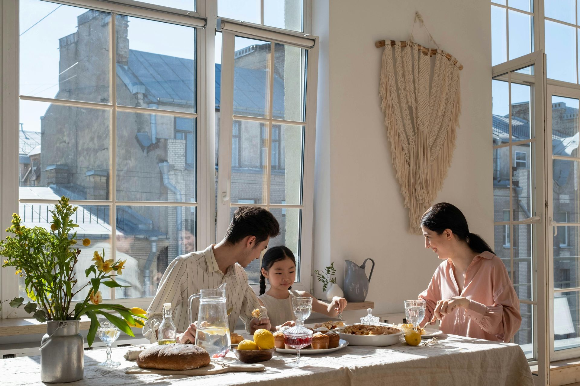 Family dining at a table by a sunny window, enjoying a meal.