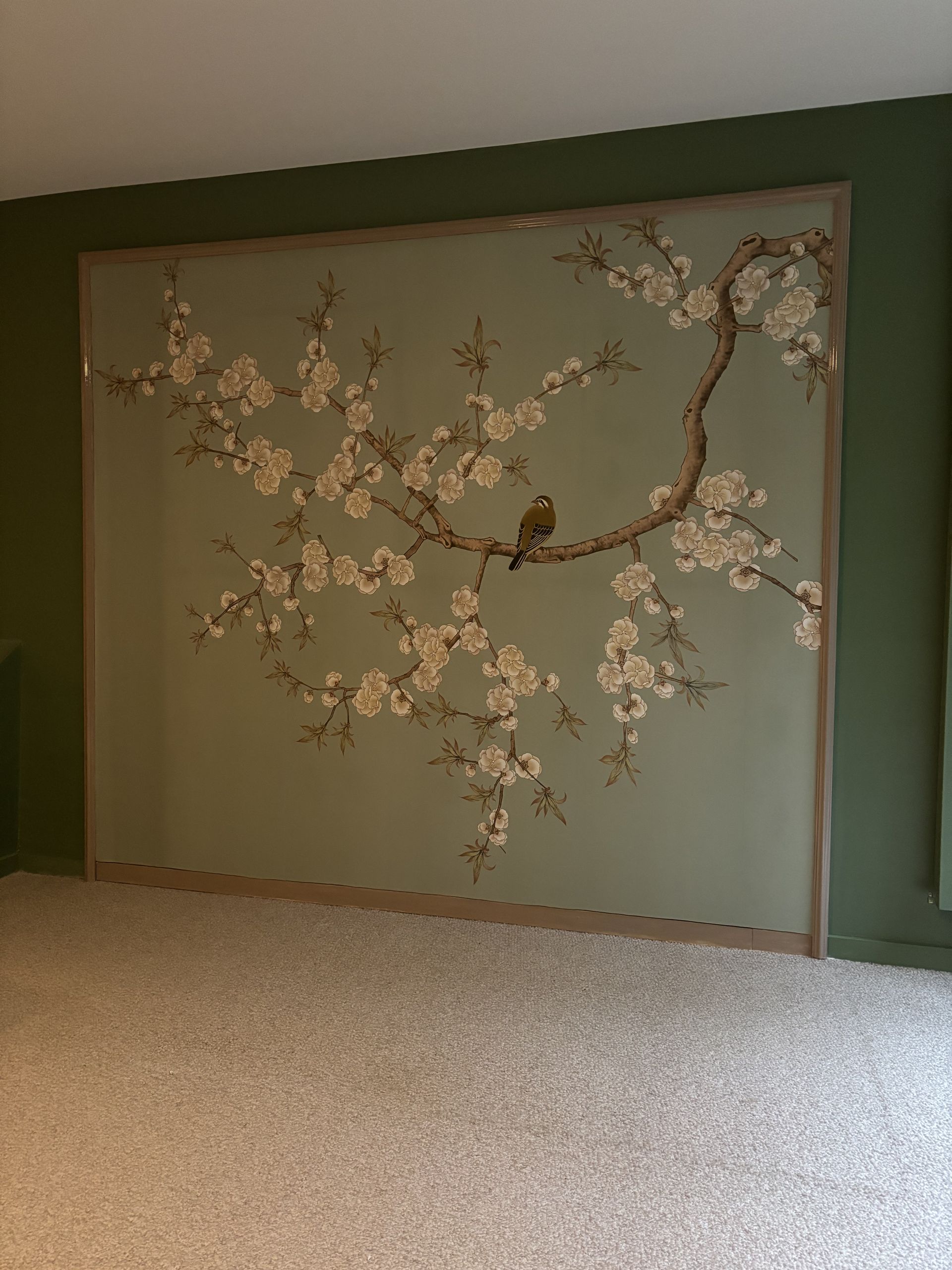 Peinture murale verte représentant une branche d'arbre en fleurs au-dessus d'un tapis beige dans une pièce