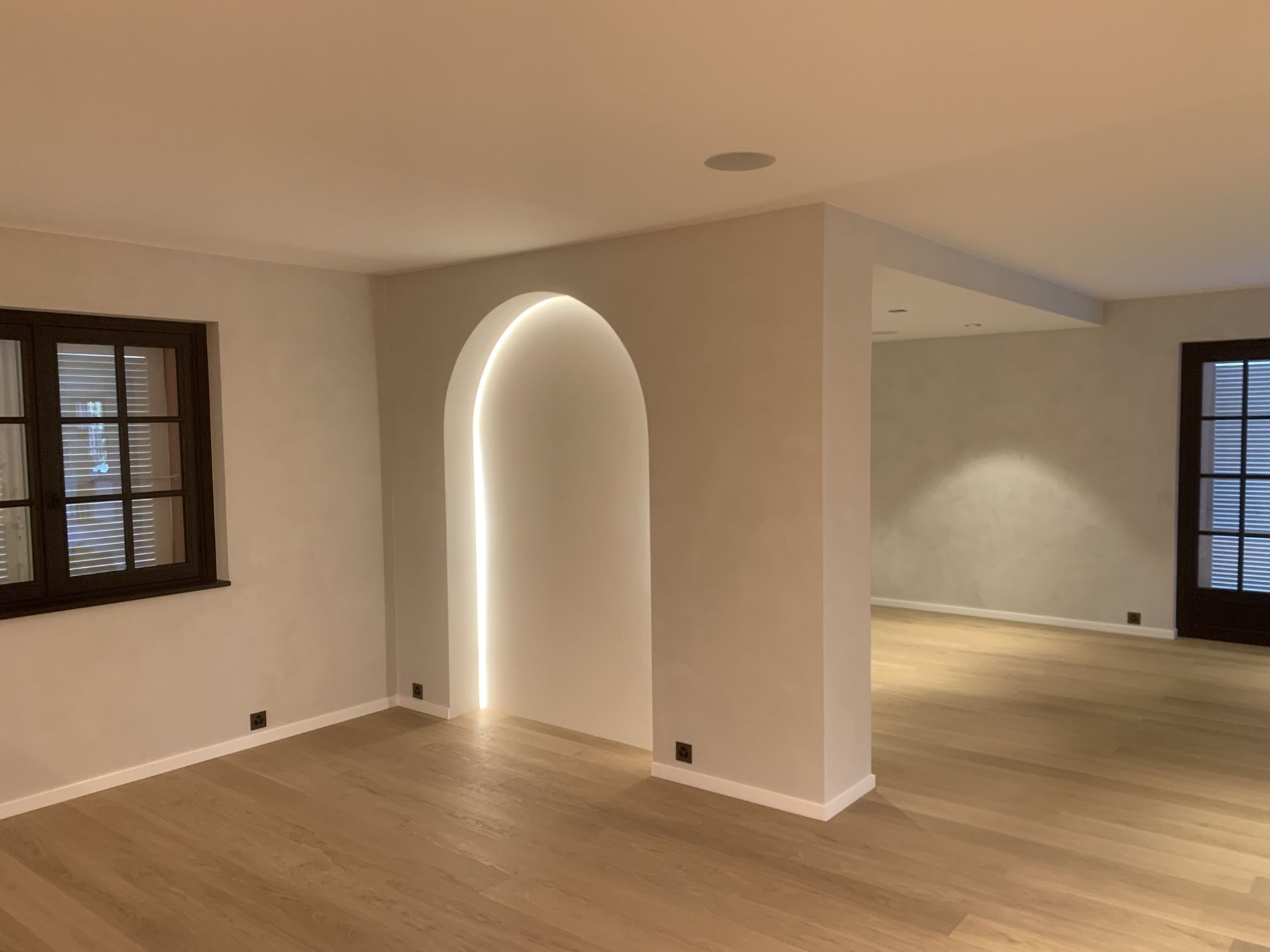 Pièce moderne vide avec parquet clair, porte cintrée et fenêtres sur murs beiges