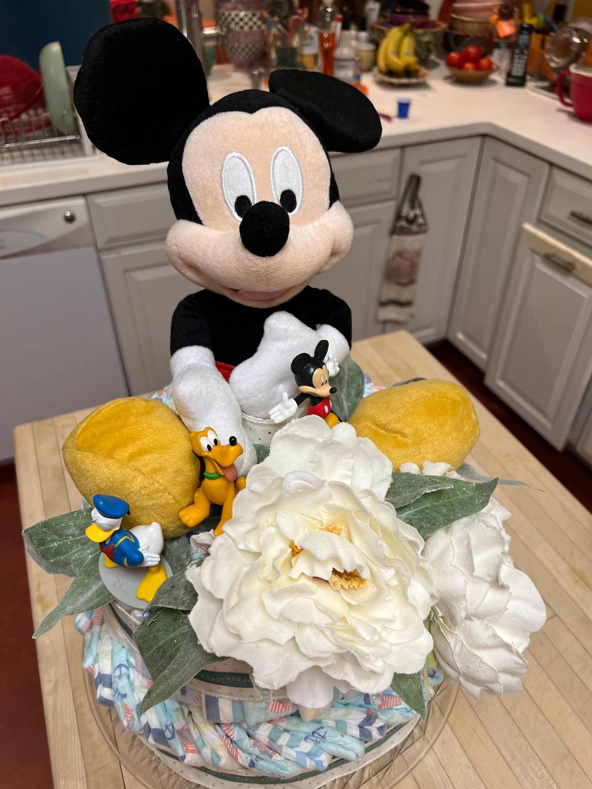 Mickey mouse figurines and white flowers on a diaper cake