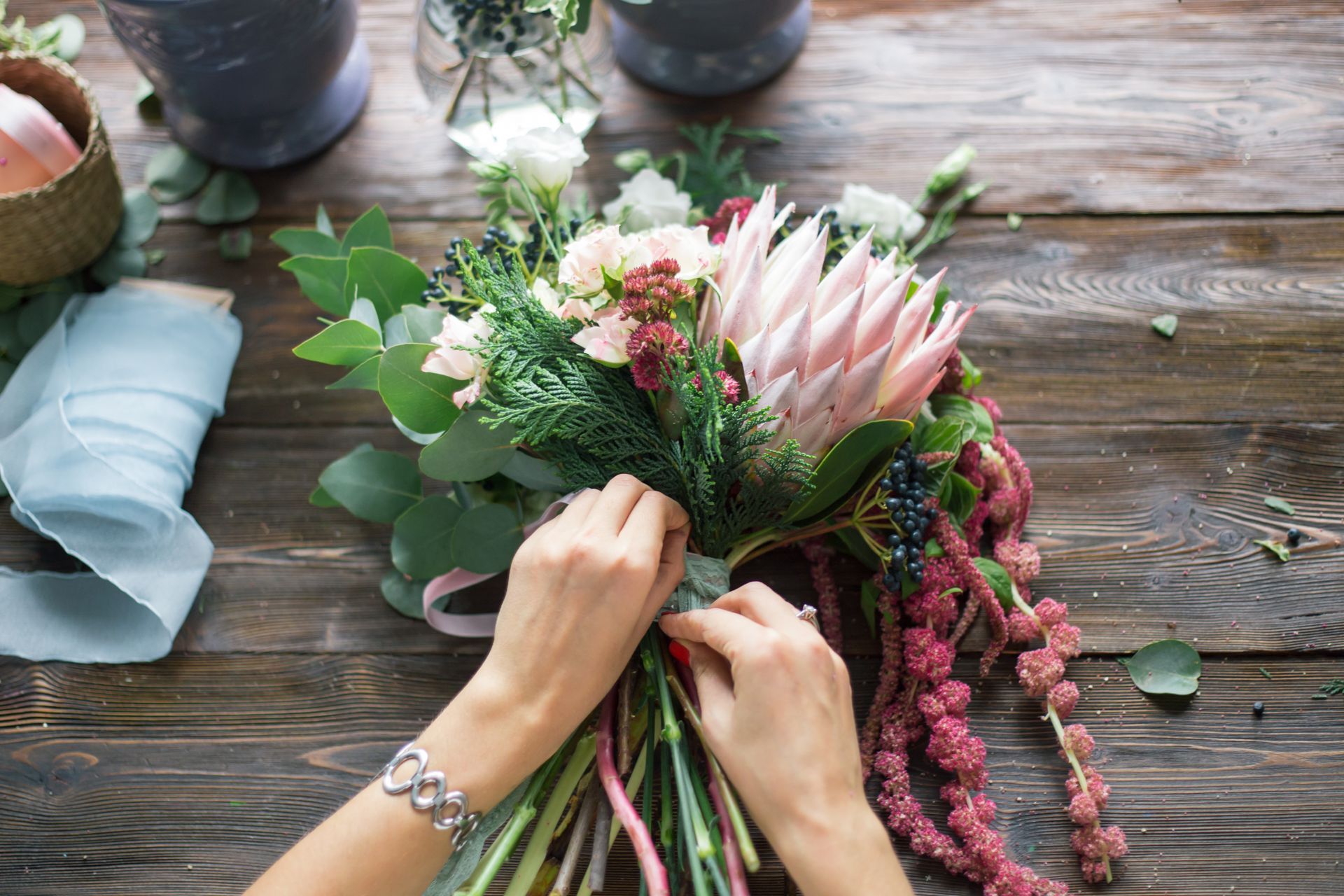 Hands arranging a pink-and-green flower bouquet on a rustic wooden table Hands arranging a pink-and-green flower bouquet on a rustic wooden table