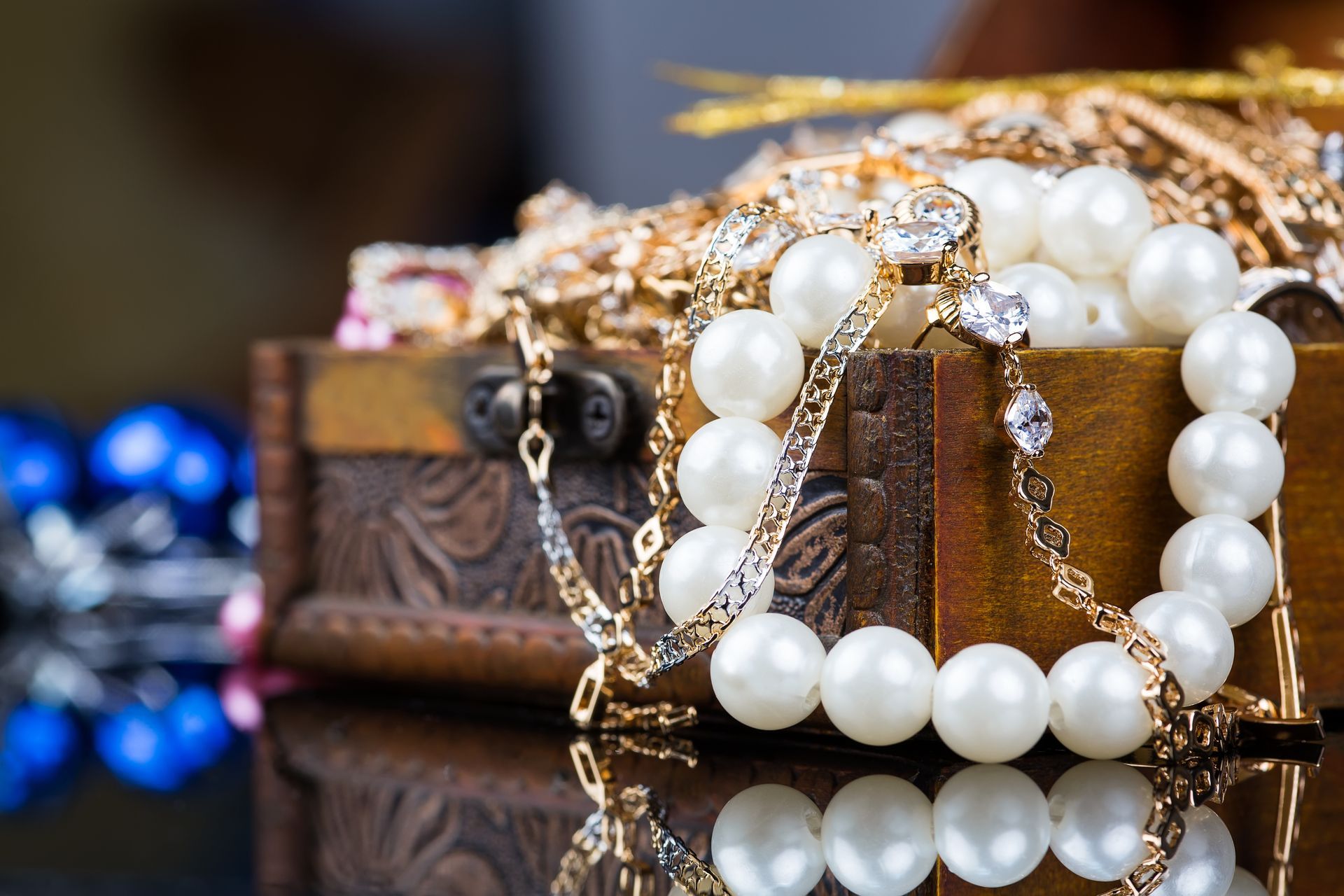 Pearl and gold jewelry draped over a small wooden chest with blue beads in the background Pearl and gold jewelry draped over a small wooden chest with blue beads in the background