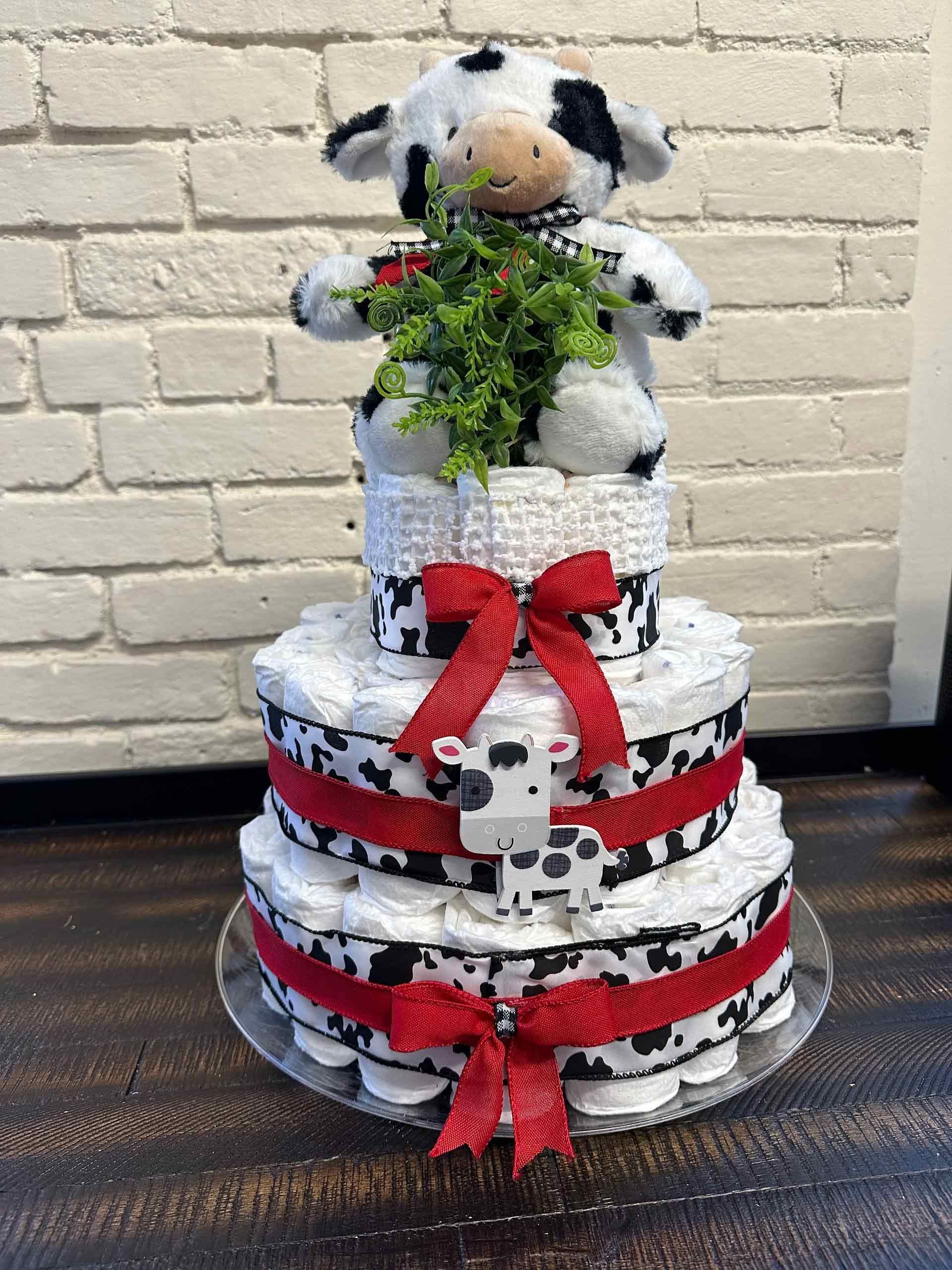 Diaper cake with cow plush, red ribbon, and greenery