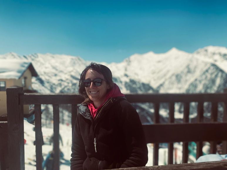Una mano che mescola un cappuccino schiumoso in una tazza nera Mado, un croissant e dei bicchieri d'acqua su un tavolo.